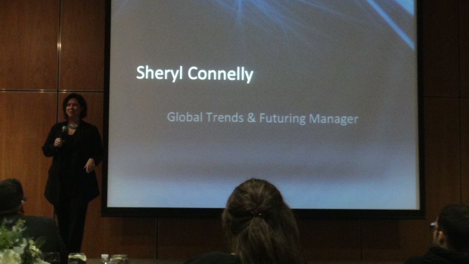 Speaker presenting on a stage with a screen displaying 'Sheryl Connelly, Global Trends & Futuring Manager'