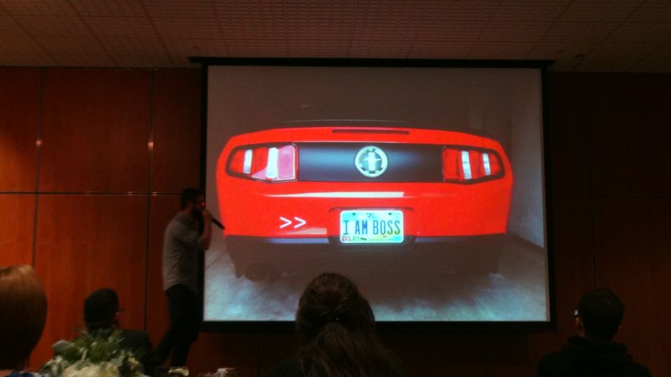 Red car's rear view, showing taillights, a circular emblem, and a license plate that reads "I AM BOSS"