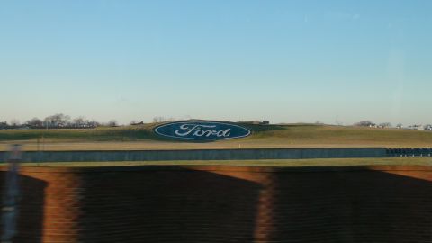 1993 Ford Taurus - The iconic Ford oval logo is visible on a hill, likely at a Ford facility, under a bright blue sky.