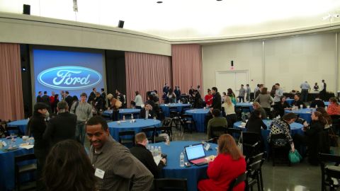 1993 Ford Taurus - A Ford logo is projected onto a large screen in a room filled with people attending an event.