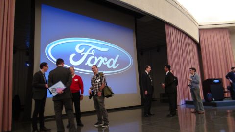 1993 Ford Taurus - A group of people stand before a large screen showing the Ford logo at an event.