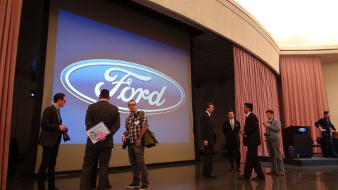 1993 Ford Taurus - Men gather in front of a large screen displaying the Ford logo during an event.