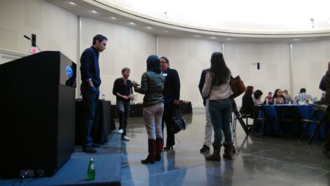 1993 Ford Taurus - A group of people are standing and talking in a large room with a podium.