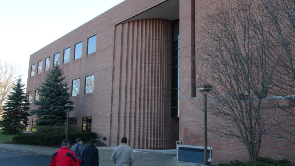 Brick building with tall windows and a curved section, people walk on the sidewalk