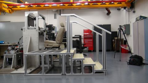 1993 Ford Taurus - A car seat is mounted on a test rig, complete with stairs and monitoring equipment, in a workshop setting.