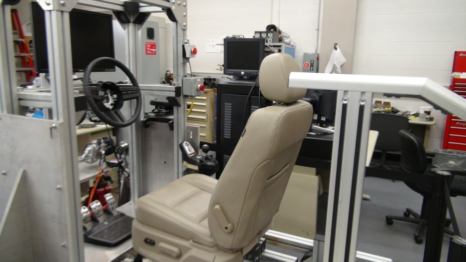 Car interior simulator with beige seat, steering wheel, and pedals