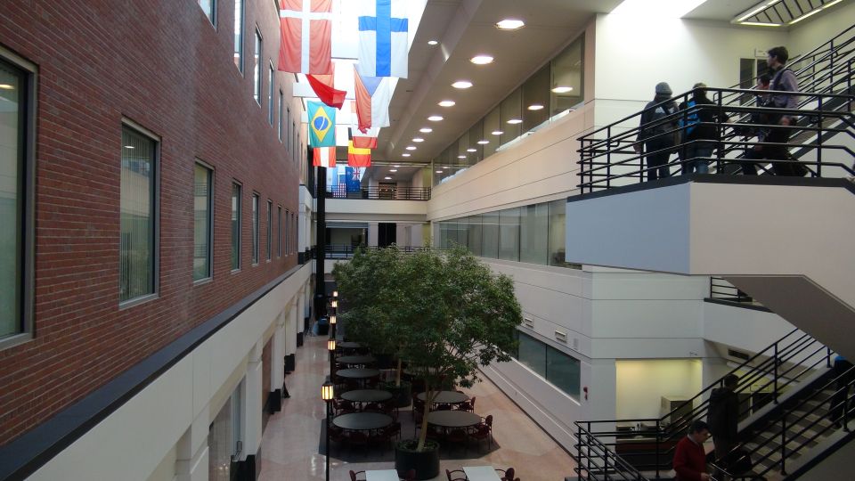 Interior atrium with flags hanging from the ceiling, tables and chairs below, and people on staircases