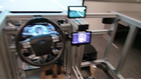 1993 Ford Taurus - A driving simulator setup features a steering wheel and multiple screens displaying driving information.