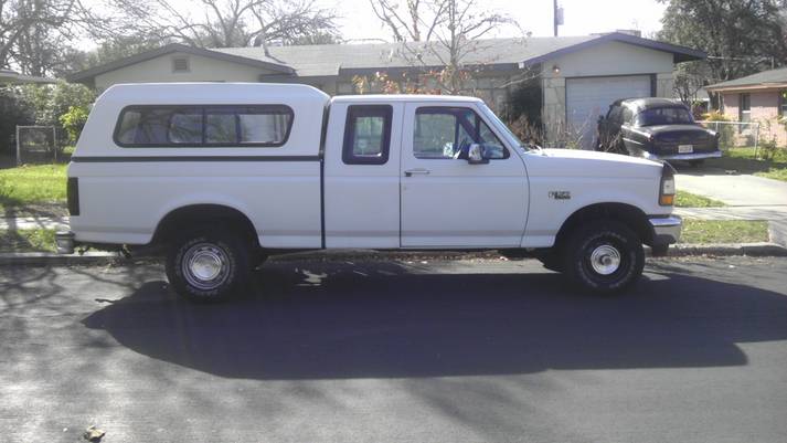 White four-door pickup truck with a camper shell, parked on asphalt.