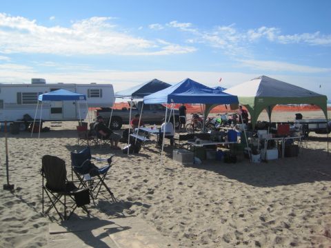 1968 Ford Bronco - A beach campsite is set up with tents, a trailer, and various equipment on a sandy shore.