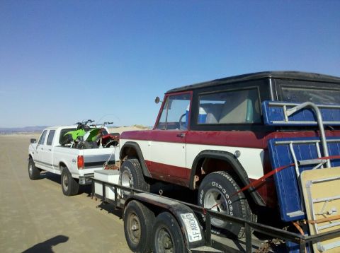 1968 Ford Bronco - A red and white 1968 Ford Bronco is towed on a trailer by a white pickup truck, with ATVs in the truck bed.
