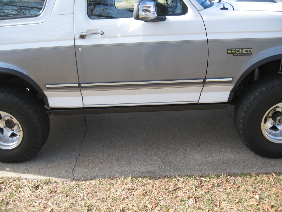 White and grey two-tone 1994 Ford Bronco side view, showing the door, fender badge, and wheels