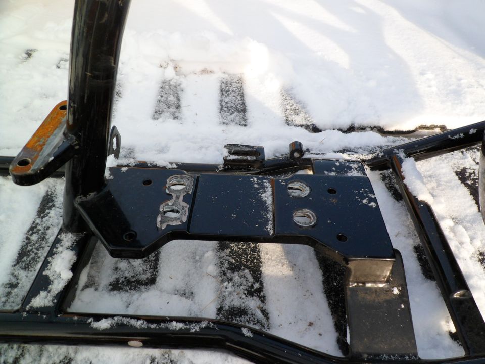 Close-up of black metal frame parts covered in snow. Some rusty metal bracket visible