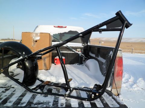 1973 Harley-Davidson Ultra - A black motorcycle frame is loaded into a snow-covered truck bed, alongside a tire and cardboard boxes.