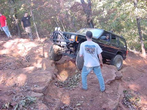 1986 Ford Bronco - A modified Jeep Cherokee navigates a challenging off-road course with steep inclines and large rocks.