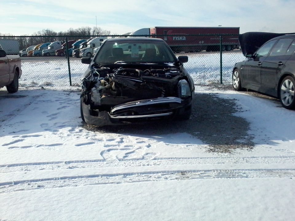 2006 Ford Fusion with front-end damage, hood open, parked in snow. Another car is parked to the right