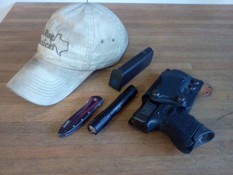 1996 Ford Bronco - A collection of personal items including a hat, knife, flashlight, handgun, and magazine are laid out on a wooden table.