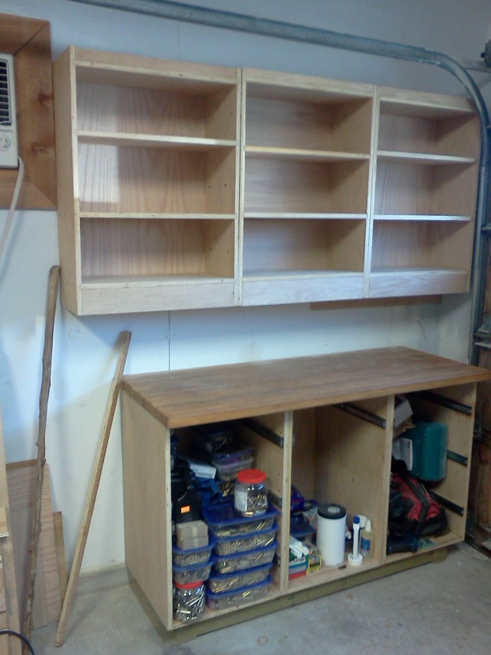 Wooden shelves mounted above a workbench filled with storage bins and supplies in a garage