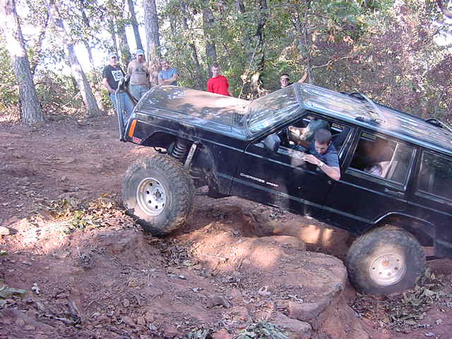 Black Jeep Cherokee XJ articulating over rock with driver leaning out the window