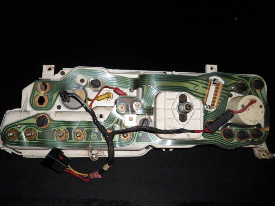 Back of a car's instrument cluster showing green circuit board traces and wiring harnesses