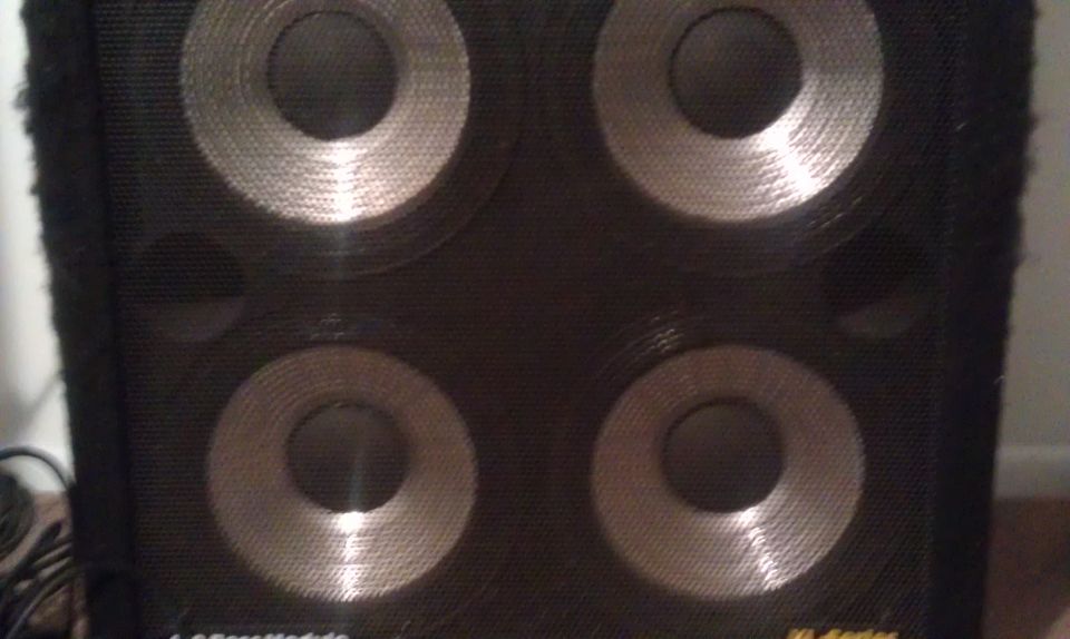 Speaker cabinet with four circular speakers and a Supermotors logo at the bottom right
