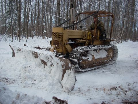 1963 Hummer H3 - Bulldozer clearing snow in a forest setting with a person operating it.