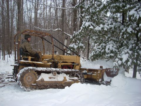 1963 Hummer H3 - A person operates a bulldozer to clear snow in a wooded area during winter.