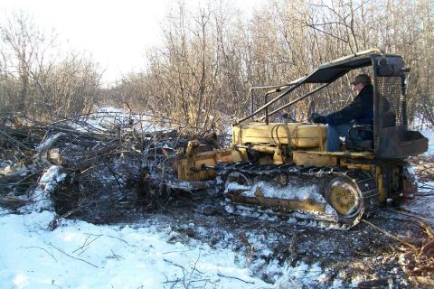 1963 Hummer H3 - A person operates a yellow crawler tractor to clear brush in a snowy, wooded environment.