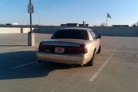 2000 Mercury Grand Marquis - A gold Mercury Grand Marquis is parked in a lot with an American flag flying in the background.