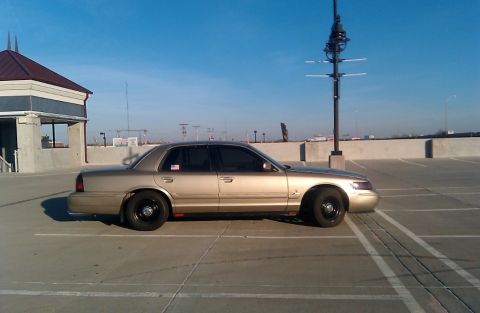 2000 Mercury Grand Marquis - Side view of a gold 2000 Mercury Grand Marquis parked in an outdoor lot under a clear blue sky.