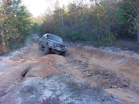 1986 Ford Bronco - Two SUVs navigate a challenging dirt path during an off-road excursion.