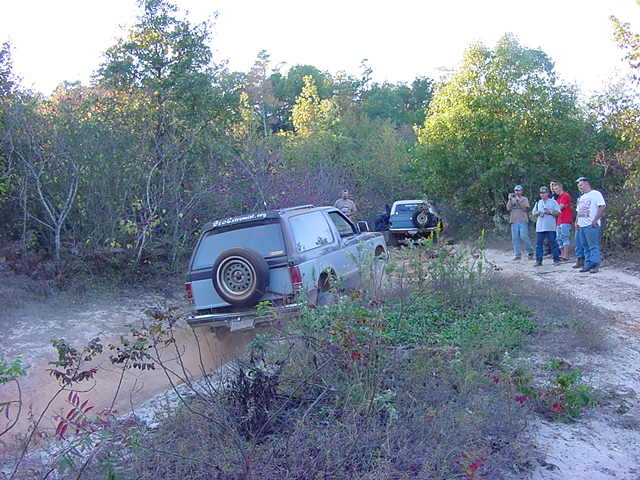Gray S-10 Blazer with tailgate spare tire dropping into a muddy hole on a trail
