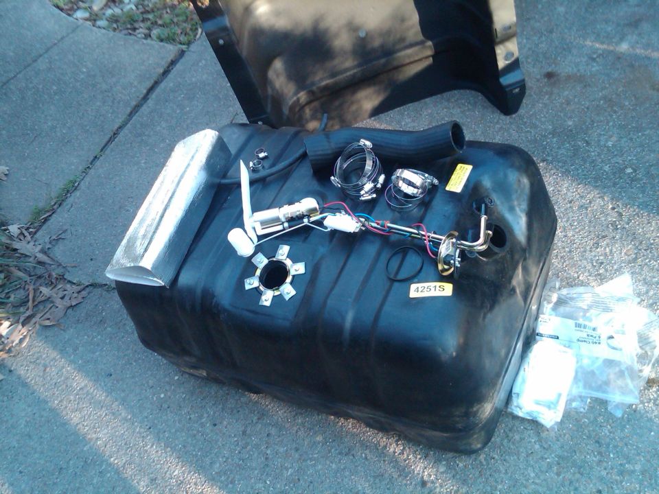 Fuel tank assembly with fuel pump, sender, and hose, laid out on pavement