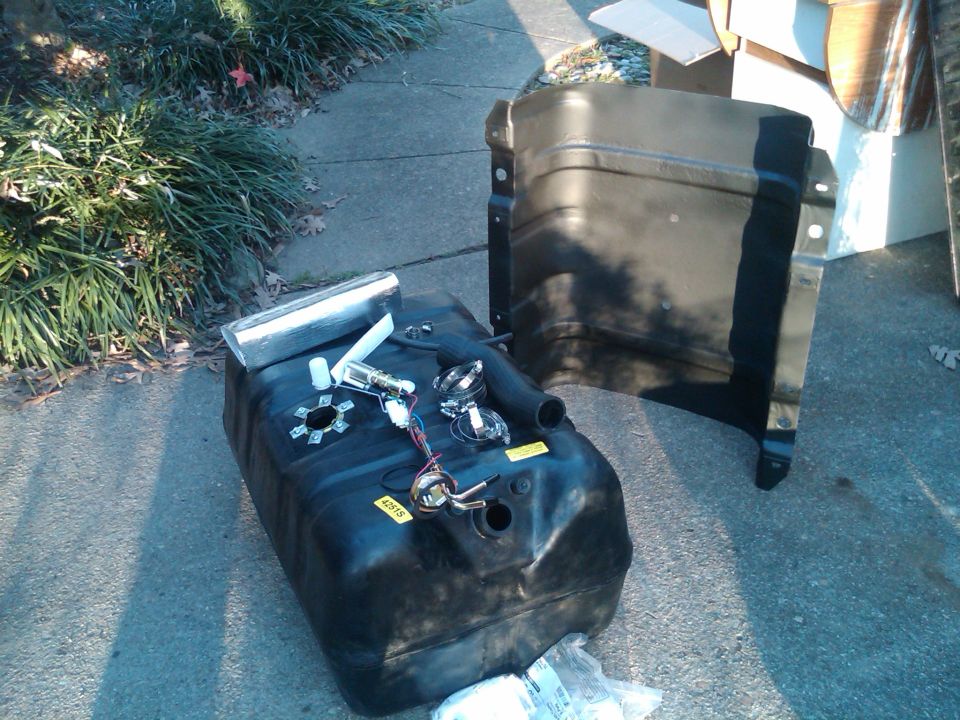 Black plastic fuel tank with fuel pump assembly and metal filler neck, next to a black metal fender liner