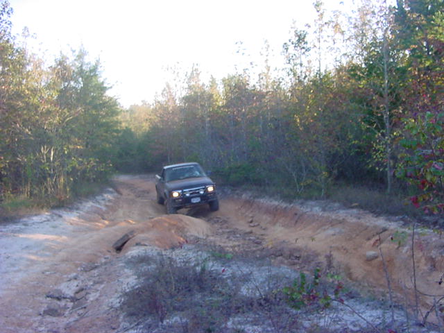 Dark compact 4x4 pickup with brush guard on a rutted sandy clay trail
