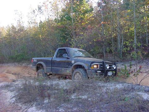 1986 Ford Bronco - A black pickup truck navigates a muddy, wooded trail during an off-road excursion.