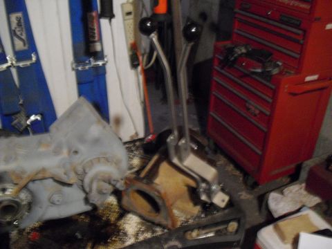 1986 Ford Bronco - A dual-stick shifter assembly is shown in a garage setting with automotive parts and a toolbox.