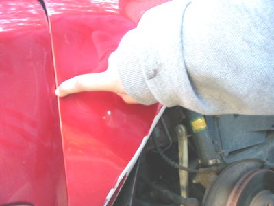 1997 Ford Taurus - A finger points to the gap between a red car's fender and door, revealing the suspension system underneath.