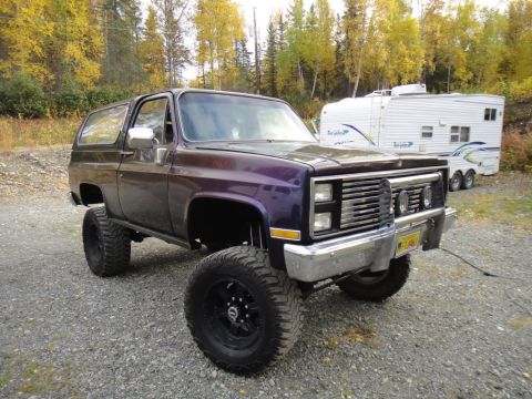 1990 Chevrolet Suburban - This lifted SUV has a custom grille and is parked outdoors with a travel trailer behind it.