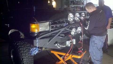 1991 Ford Bronco - A man works on wiring for auxiliary lights attached to the front bumper of a black Ford Bronco.