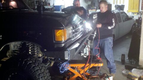 1991 Ford Bronco - Two men work on the front end of a 1991 Ford Bronco, with another vehicle visible in the background.