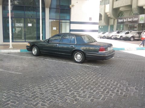 1998 Ford Crown Victoria - A dark green 1998 Ford Crown Victoria is parked in front of a building with a spa and beauty center.