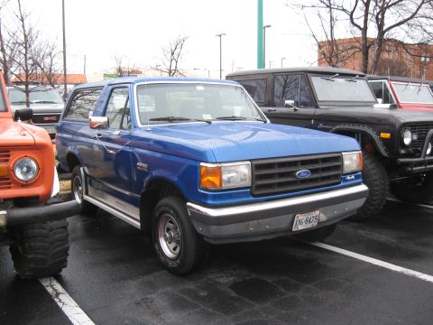 1994 Ford Bronco - A blue Ford Bronco is parked in a lot with other vehicles visible.