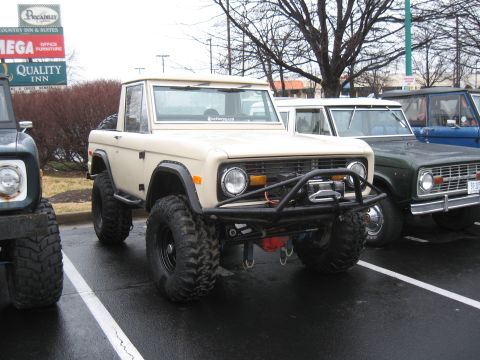 1994 Ford Bronco - Several Ford Broncos are parked in a lot, with a tan one in the foreground off-road modifications.