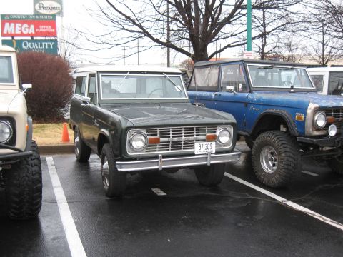 1994 Ford Bronco - A green Ford Bronco is parked next to a blue Ford Bronco in a parking lot.