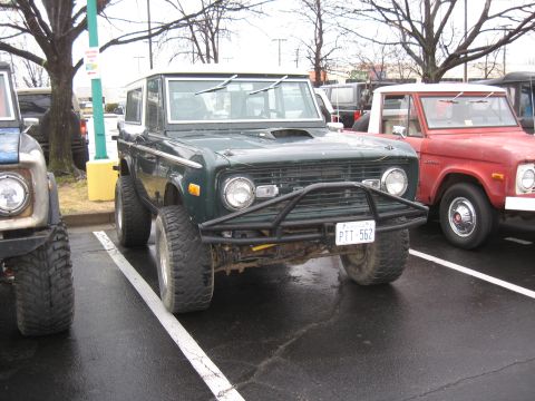1994 Ford Bronco - Two Ford Broncos, a first-gen and a second-gen, parked in a lot. The first-gen has a brush guard.
