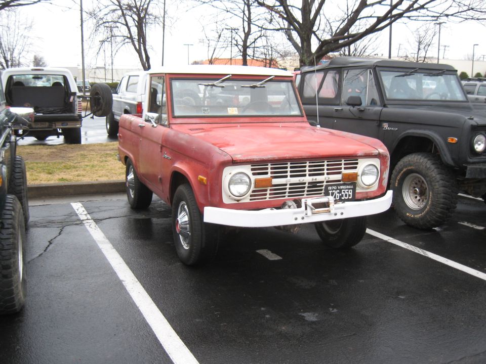 Red first-gen Ford Bronco parked next to a black Bronco. License plate reads T26-559