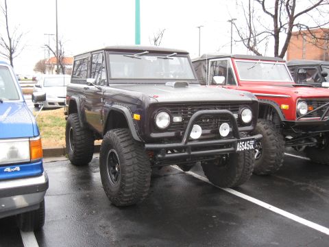 1994 Ford Bronco - A dark purple Ford Bronco is parked next to a red Bronco and a blue truck.