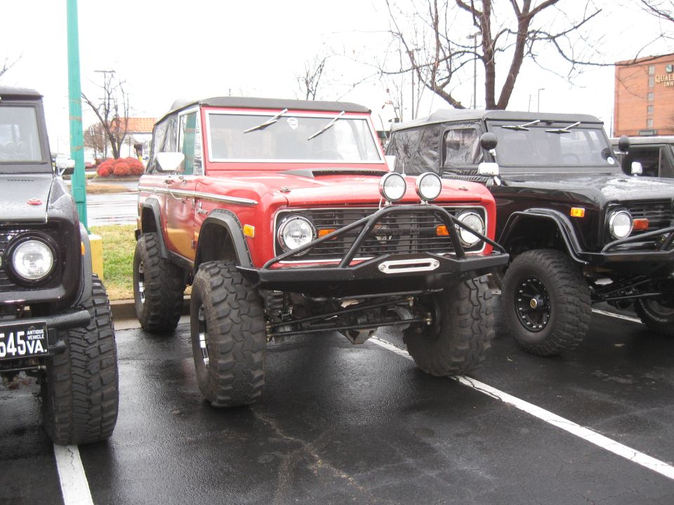 Red 1978 Ford Bronco with bull bar and large tires parked next to other Broncos
