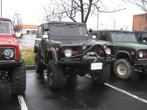 1994 Ford Bronco - Several first-generation Ford Broncos are parked together in a lot, one black and one to its right with a green hood accent.